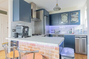 A modern kitchen with blue cabinets, a gas stove, a coffee machine, and a dishwasher. - 2BDR Hidden Gem in the Heart of Clapham (London)