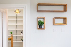 A room with a white door, a hanging light fixture, and three wooden wall shelves with various items. - 2BDR Hidden Gem in the Heart of Clapham (London)