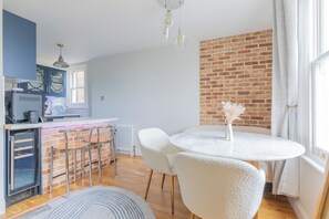 A modern kitchen with a brick accent wall, a dining area with a round table and chairs, and a view of the outdoors. - 2BDR Hidden Gem in the Heart of Clapham (London)