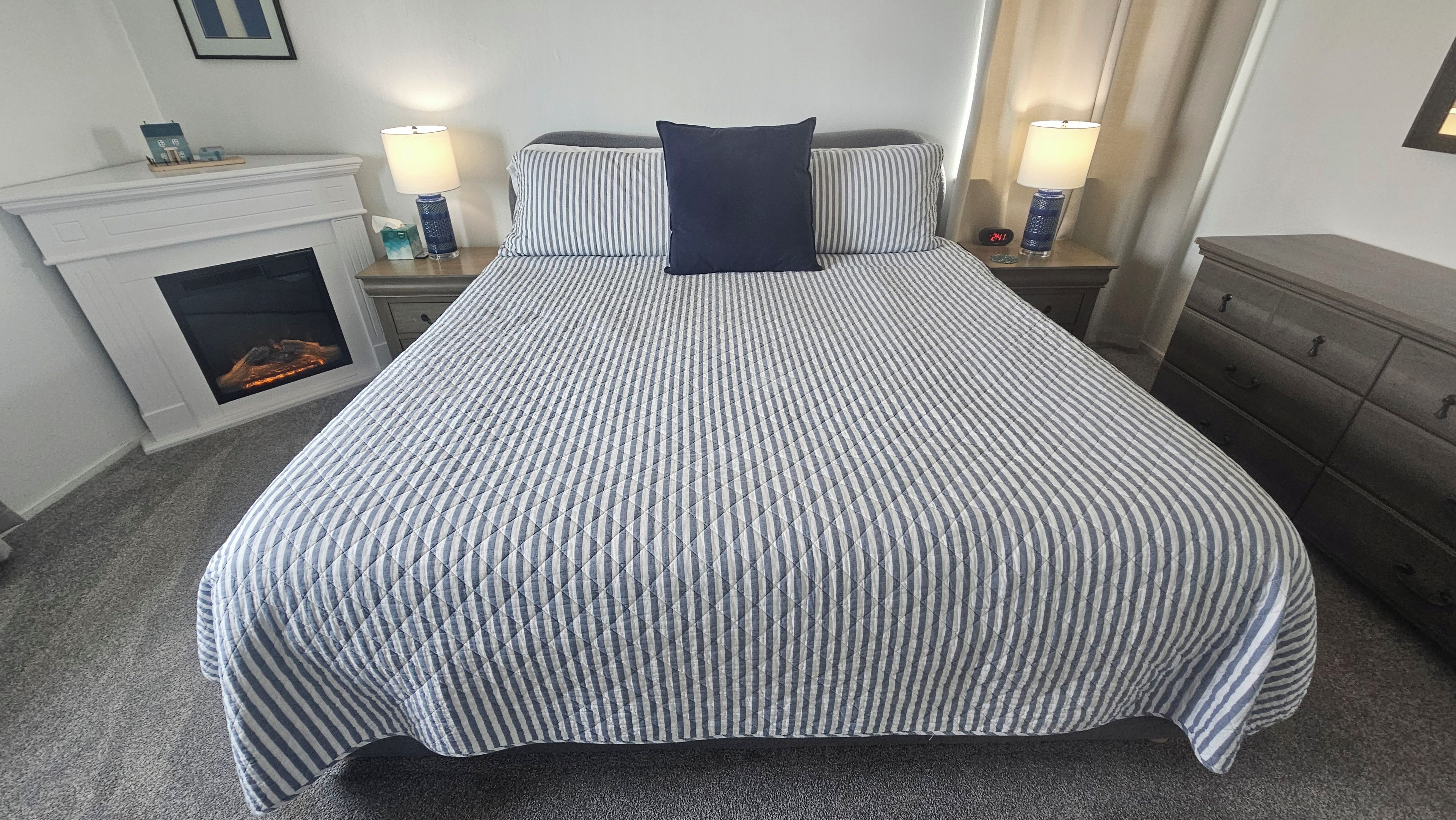 Cama bem arrumada com colcha listrada e um único travesseiro escuro.