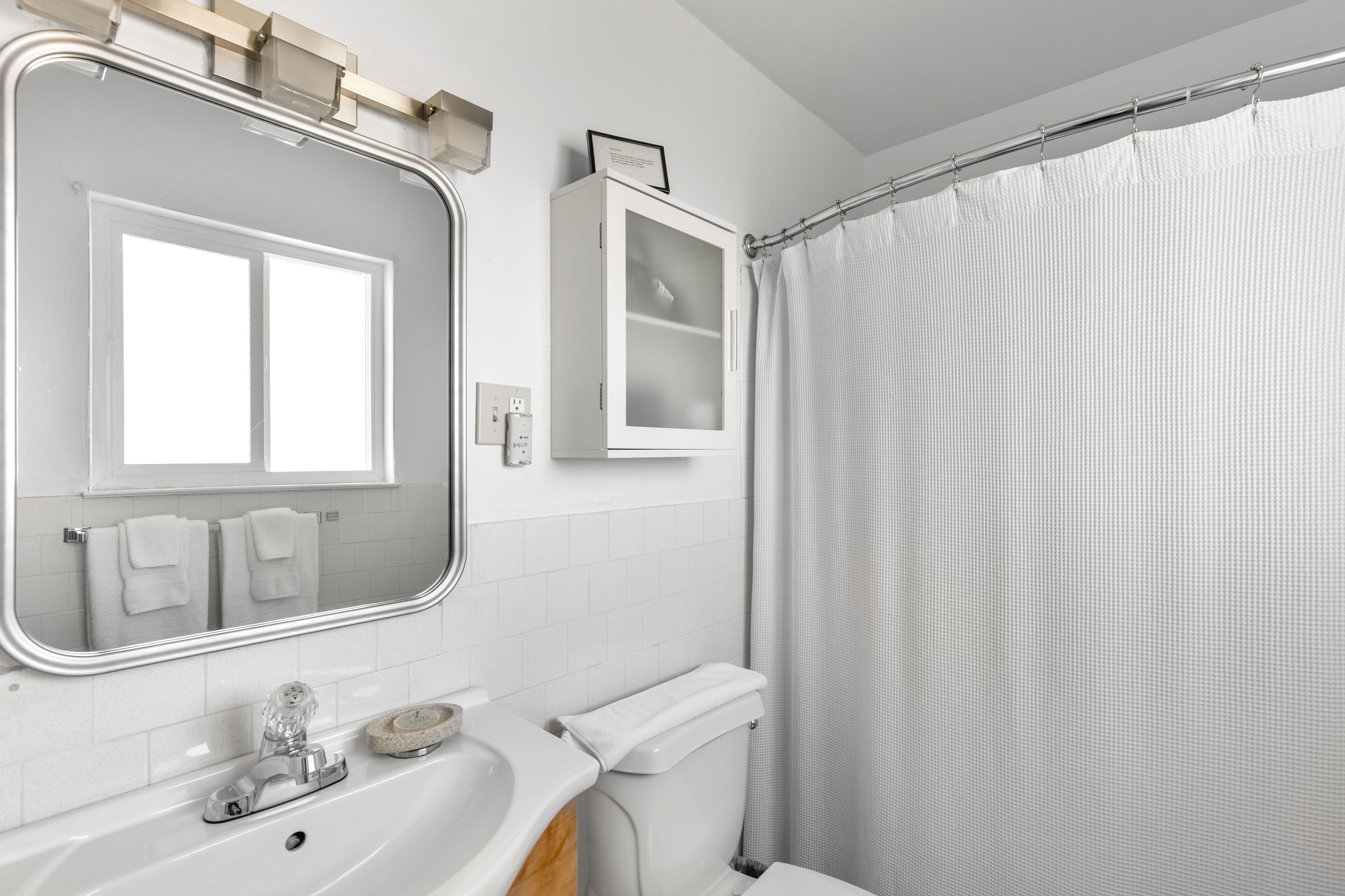 A modern bathroom with a large mirror, a white sink, a toilet, and a shower curtain.