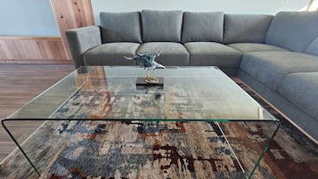 A living room with a glass-top coffee table, a patterned rug, and a grey sofa.