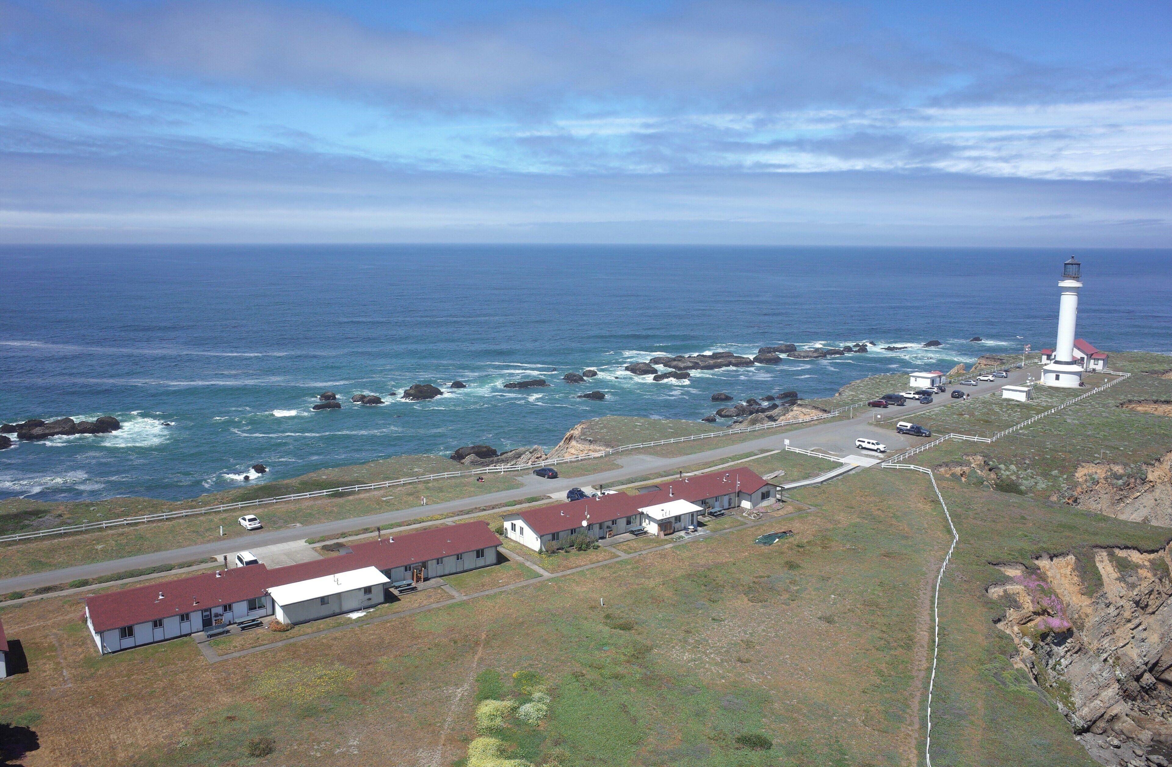 Une zone côtière comprenant un phare, une côte rocheuse et une route menant à un ensemble de bâtiments.