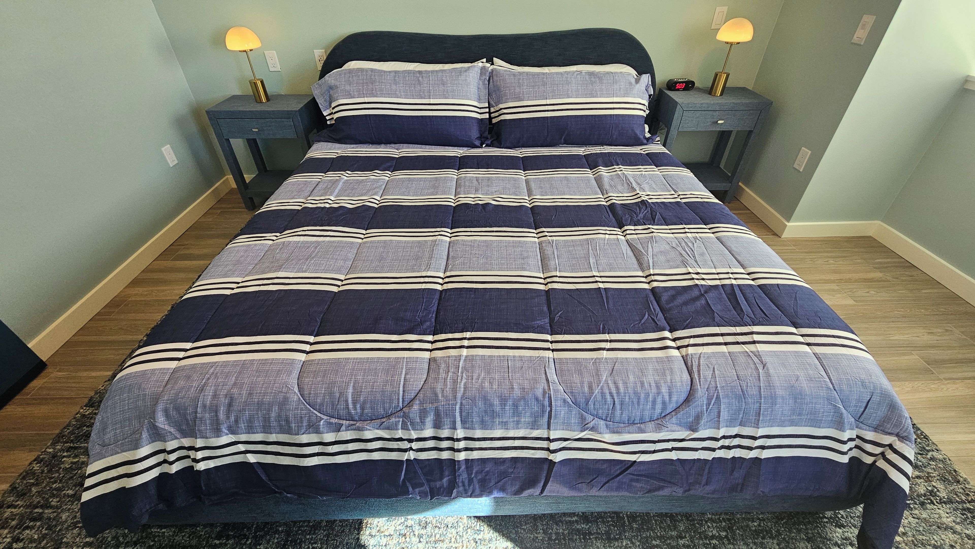 A bed with a striped bedspread, two bedside tables with lamps, and a clock on one of the tables.