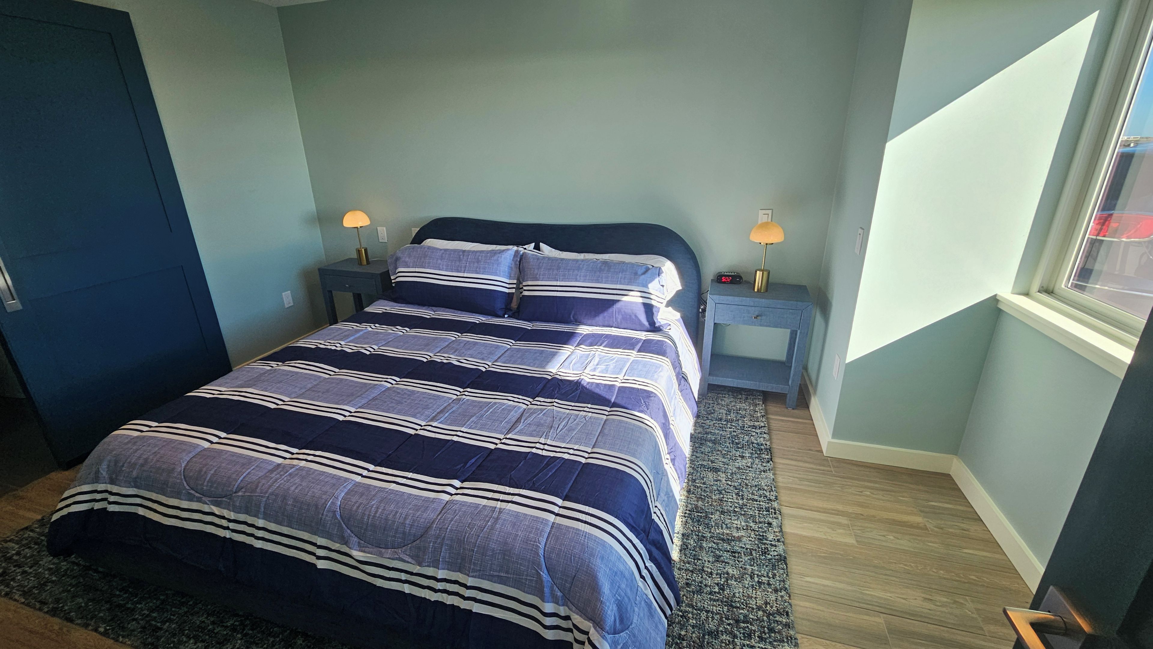 A bedroom with a bed, nightstands, a lamp, and a window.