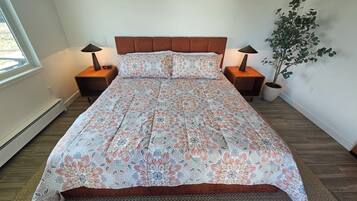 A bedroom with a bed, two bedside tables, a nightstand, a potted plant, and a window.