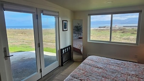 A room with a bed, a window with a view of the sea, and a door leading to an outdoor area. - Point Arena Lighthouse - Humpback Whale Cottage (Point Arena)