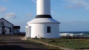 A white lighthouse with a black top, situated next to a building with a small porch. - Point Arena Lighthouse - Assistant Keeper's House 3 (Point Arena)