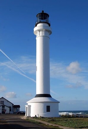 A white lighthouse with a black top, situated next to a building with a small porch. - Point Arena Lighthouse - Assistant Keeper's House 3 (Point Arena)