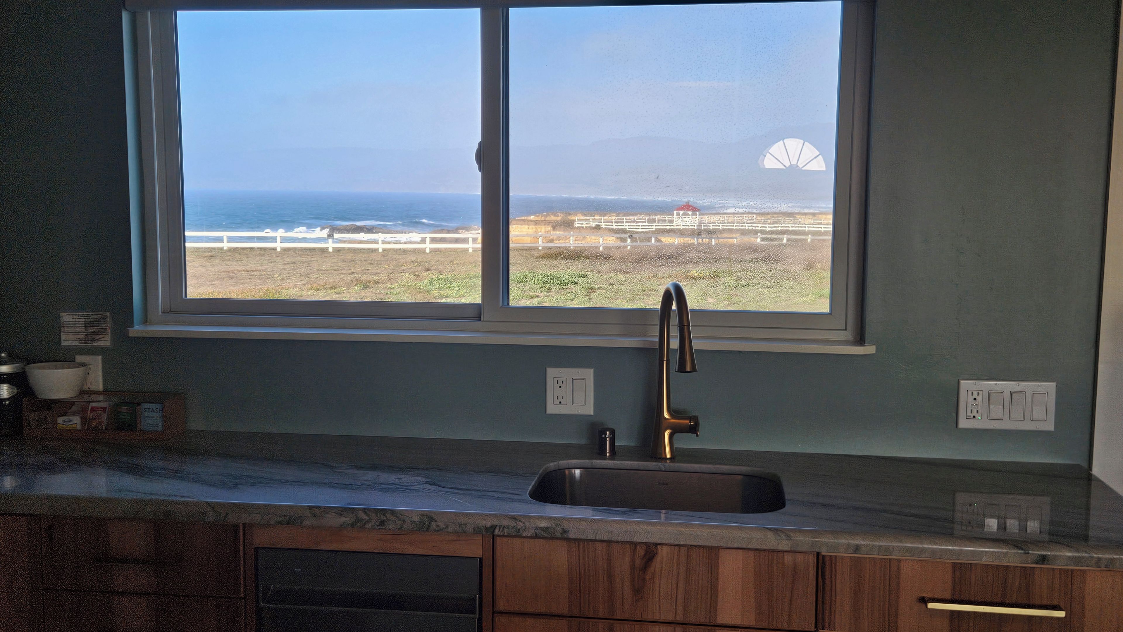 A kitchen with a window overlooking a beach and a windmill.