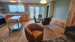 A modern kitchen with a dining area, a large window, and a view of the outdoors. - Point Arena Lighthouse - Humpback Whale Cottage (Point Arena)