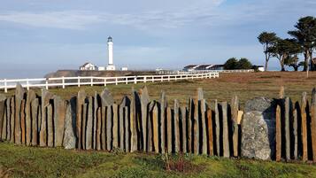 A coastal landscape with a lighthouse, white fence, and houses in the background.