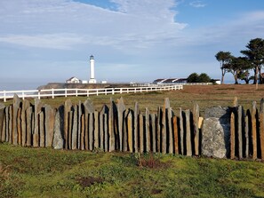 A coastal landscape with a lighthouse, white fence, and houses in the background. - Point Arena Lighthouse - Assistant Keeper's House 3 (Point Arena)