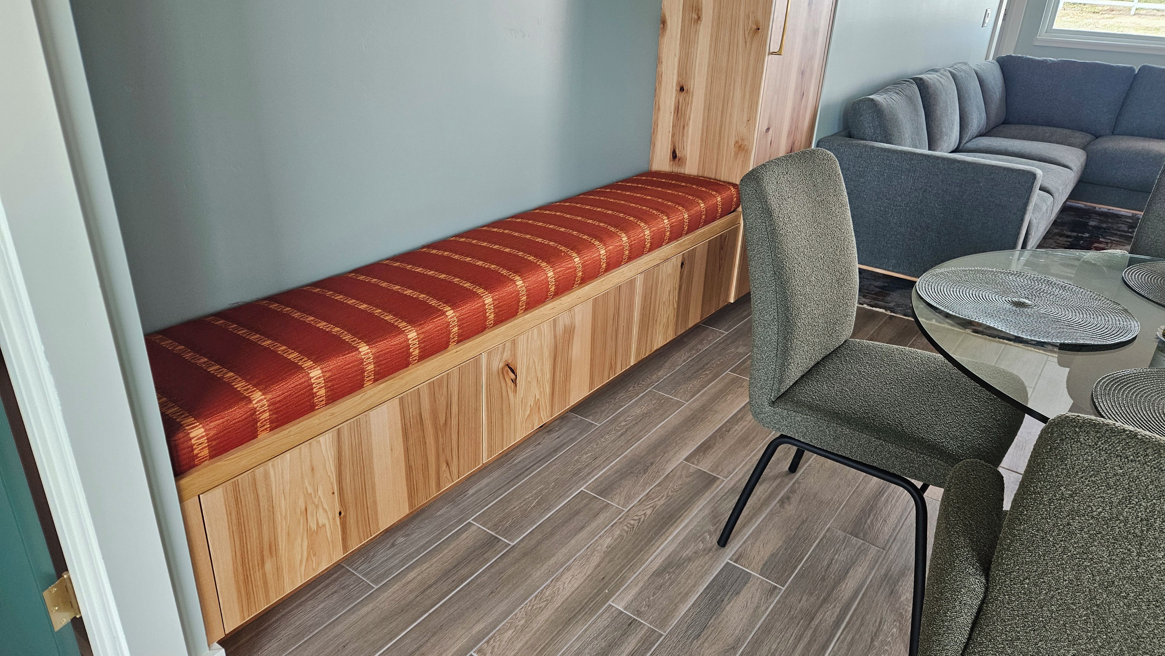 Et værelse med en træbænk, et spisebord med en rund glasplade og en grå sofa.