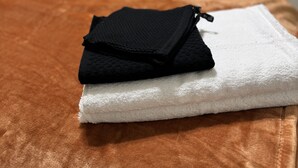 Een netjes opgemaakt bed met een bruine plaid, een wit kussen en een zwart kussen. Een zwart kledingstuk ligt op een witte handdoek op het bed.