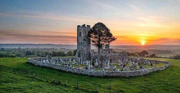 A historic stone structure with a central tower and a surrounding circular wall, set in a grassy field. - Renovated farmhouse rural setting,1km from Co Meath village (Oldcastle)