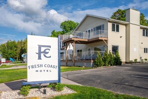 A motel sign with the name "Fresh Coast Motel" and a building with a balcony and a covered parking area. - The Deckhouse | Water Views, Walk Downtown, Sauna (Fish Creek)