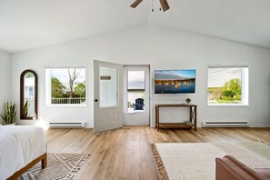 A bedroom with a bed, a desk, and a TV. There are windows and a door. - The Deckhouse | Water Views, Walk Downtown, Sauna (Fish Creek)