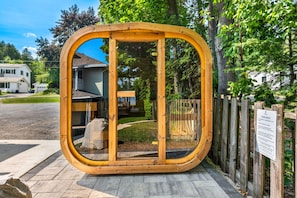 A sauna structure with a wooden frame and glass doors, surrounded by a wooden fence and a sign with rules. - The Deckhouse | Water Views, Walk Downtown, Sauna (Fish Creek)