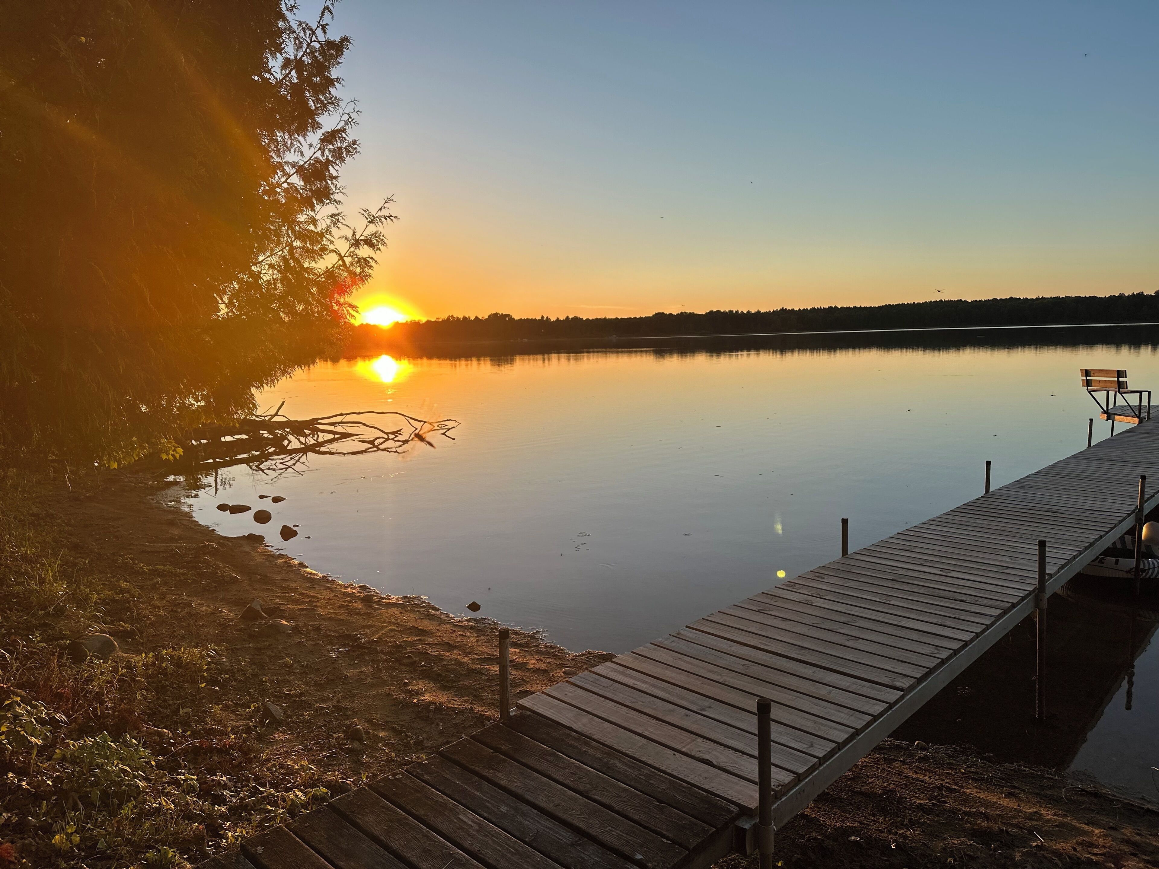 Puinen laituri, joka ulottuu tyynelle järvelle, ja taustalla auringonlasku.