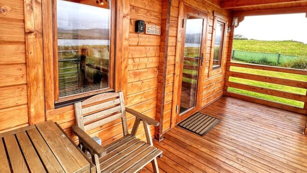 A wooden cabin with a covered porch, wooden benches, and a sign indicating a cabin number. - Harlosh Log Cabins, Cabin No 2 (Dunvegan)
