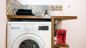 A compact laundry area with a washing machine, a shelf with a Revlon box, and a patterned tile backsplash. - Central Part-Dieu - Apartment 1 (Lyon)