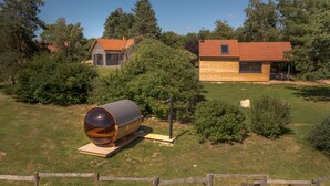 A modern house with a wooden exterior, a large cylindrical structure in the foreground, and a well-maintained garden. - Lodge Cèdre Private Spa and Sauna, in a Green Environment, View of the Morvan (BRAZEY EN MORVAN)