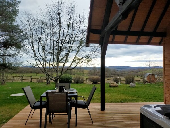 An outdoor patio with a table and chairs, overlooking a grassy landscape with trees and hills.