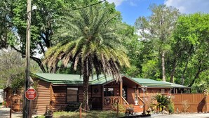 A rustic log cabin with a green roof, a porch, and a stop sign nearby. - Riverside Lodge Resort (Inverness)