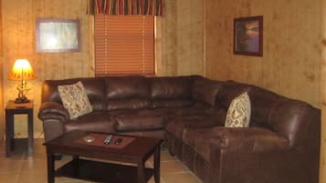 A living room with a brown leather sectional sofa, a small wooden coffee table, a lamp, and a framed picture on the wall.