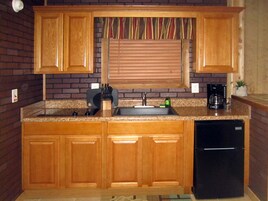 Una cocina con armarios de madera, un refrigerador negro, un lavamanos y una ventana con persianas.