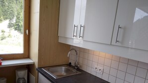 Una cucina moderna con lavello in acciaio inox, mobili bianchi e una finestra che dà su del verde.