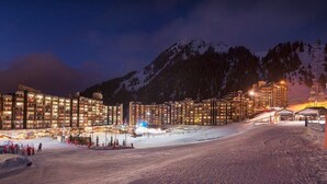 Pista da sci innevata con edifici illuminati sullo sfondo.
