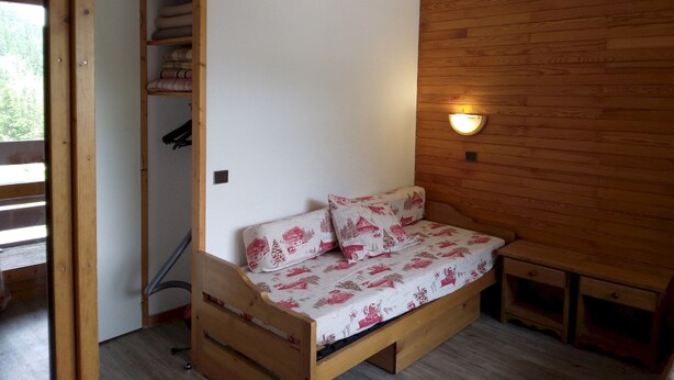 Una stanza piccola e accogliente con un letto di legno, una mensola a muro e un lampadario.
