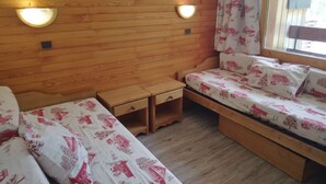 Una stanza accogliente con pareti in legno, due comodini, un letto con lenzuola a motivi floreali e due luci fissate al muro.