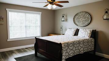 Une chambre à coucher comprenant un lit, un ventilateur de plafond, une fenêtre avec des stores, une table de chevet et des œuvres d'art décoratives sur les murs.