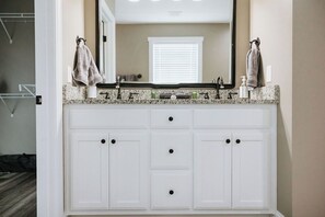A bathroom with a white vanity, a large mirror, and a window with blinds.