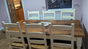 A dining area with a wooden table and white chairs, a window with a view, and a door leading to a kitchen. - 2 Bed House - Garden & Excellent Wifi (Newark)