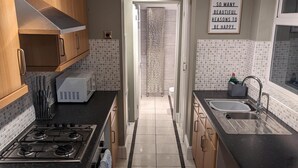 A kitchen with wooden cabinets, a gas stove, a microwave, and a sink. - 2 Bed House - Garden & Excellent Wifi (Newark)