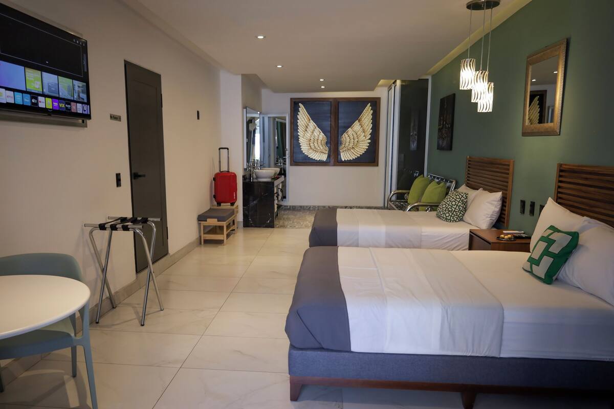 Une chambre d’hôtel avec deux lits, un bureau, une chaise, une télévision, une salle de bain avec un miroir et un mur décoré de motifs ailés.