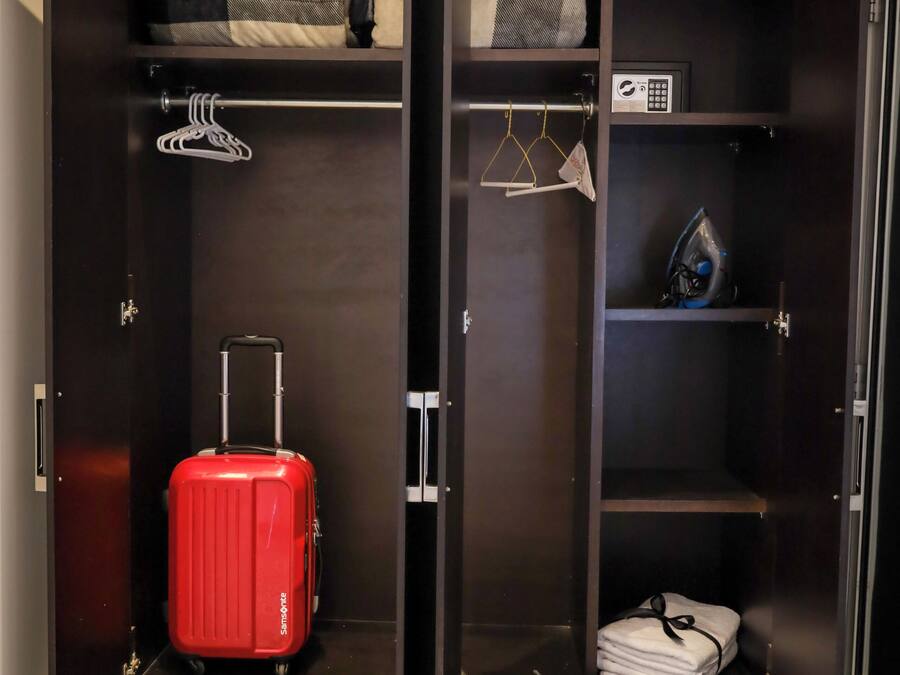 A walk-in closet with a suitcase, hanging clothes, and a microwave.