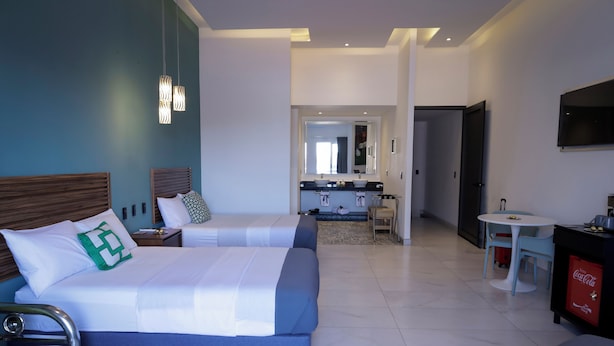 Une chambre d’hôtel avec deux lits, une salle de bain avec un lavabo et un miroir, une petite table avec des chaises et un téléviseur fixé au mur.
