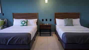A hotel room with two beds, each with a wooden headboard, white bedding, and a small bedside table with a lamp.