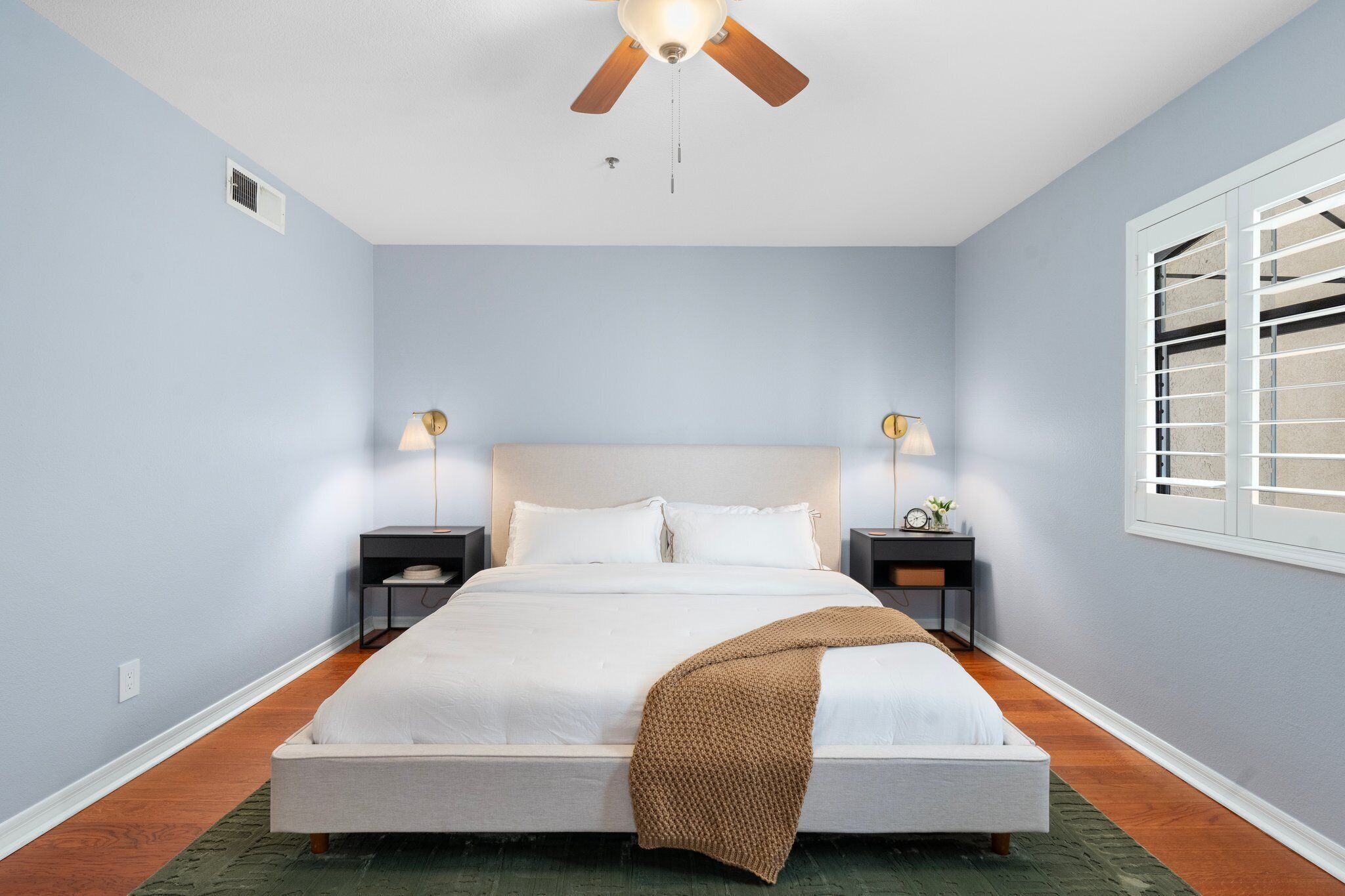 Ein Schlafzimmer mit Bett, Nachttischen, Deckenventilator und einem Fenster mit Jalousien.