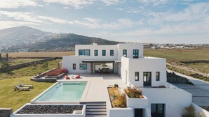 A modern house with a pool, outdoor seating, and a view of the surrounding landscape.