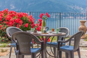 A round table with chairs, a vase with flowers, and a coffee pot. - Golden View Apartment (Perledo)