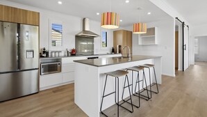 A modern kitchen with a large island, stainless steel appliances, and striped pendant lights. - House Naomi - Martinborough Holiday Home (Martinborough)