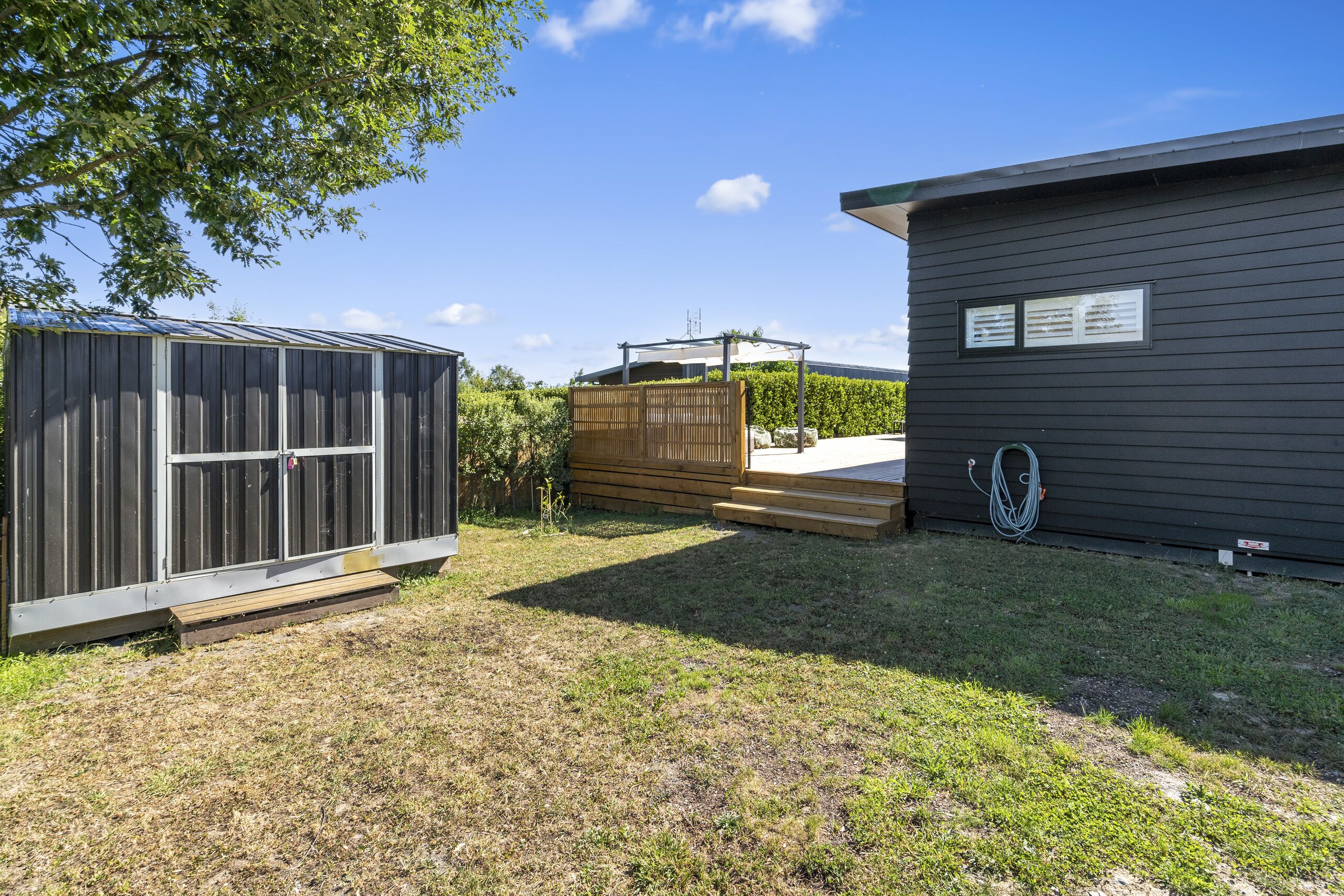 A backyard with a wooden shed, a small house, and a fenced area.