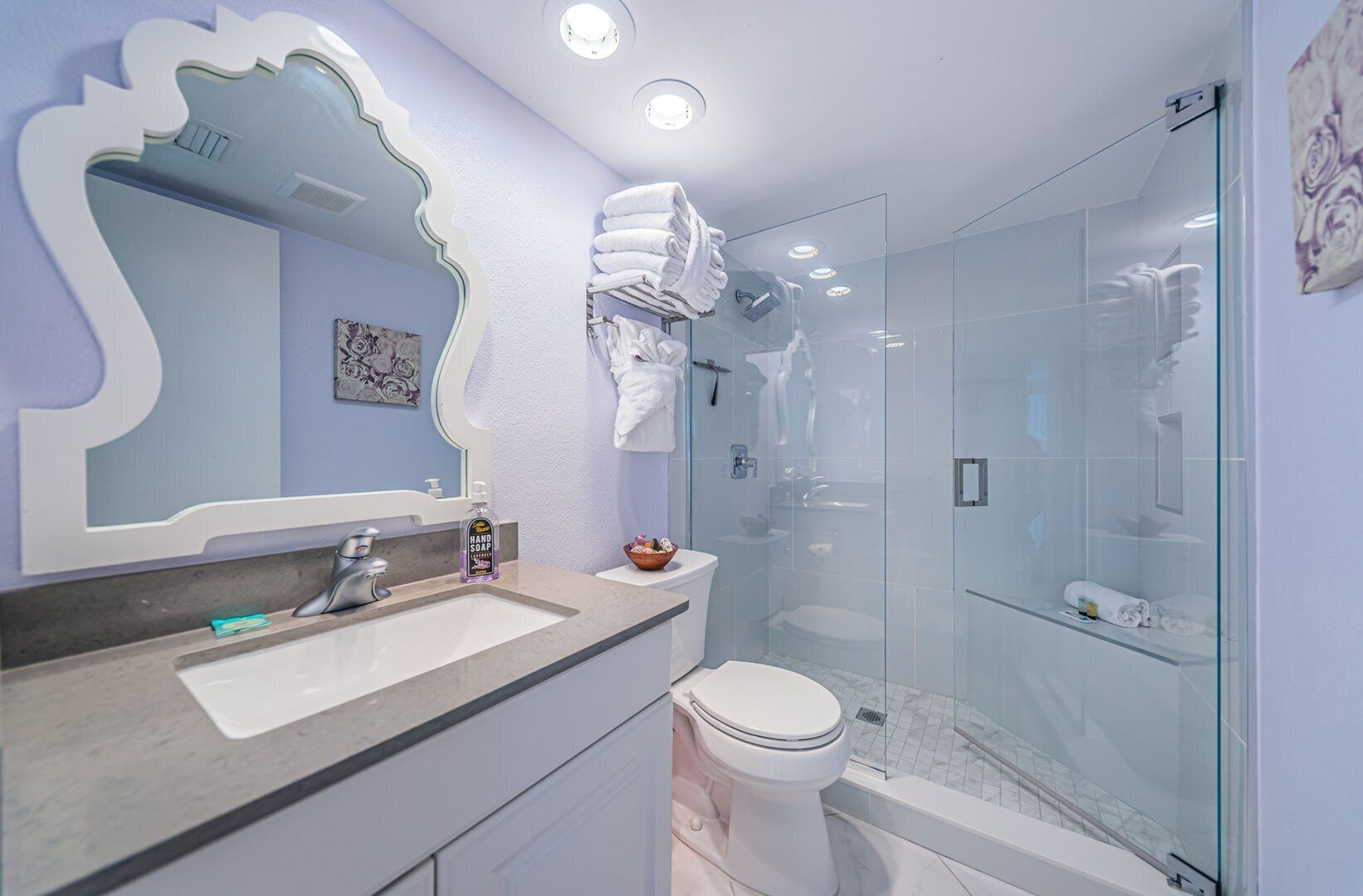 Et moderne badeværelse med et toiletbord, vask, spejl og en brusekabine med glasvægge.