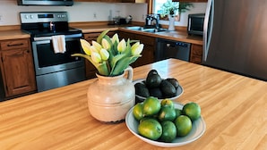 Una cocina con armarios de madera, electrodomésticos de acero inoxidable, un jarrón con flores y un tazón con limones y aguacates sobre la encimera.